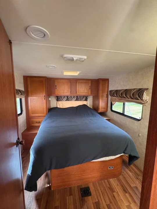 Comfortable RV rental bedroom featuring a large bed, warm wood cabinetry, laminate flooring, and natural light.. Coachmen Freelander 2014