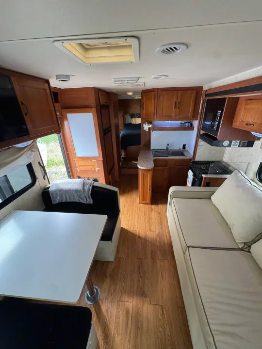 Inside this RV rental: a bright, wood-floored interior with a complete kitchen, dinette, sofa, and private bedroom beyond.. Coachmen Freelander 2014