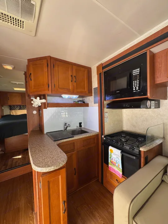 RV rental interior: A full view of a compact kitchen with a microwave, stove, sink, ample cabinets, and a partial view of the bed & sofa.. Coachmen Freelander 2014