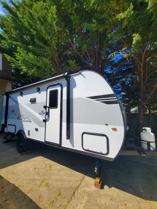 This white Jayco Baja Edition rv rental travel trailer is parked on concrete, shaded by lush green trees.. Jayco Jay Flight SLX 197MBW Baja Edition 2025