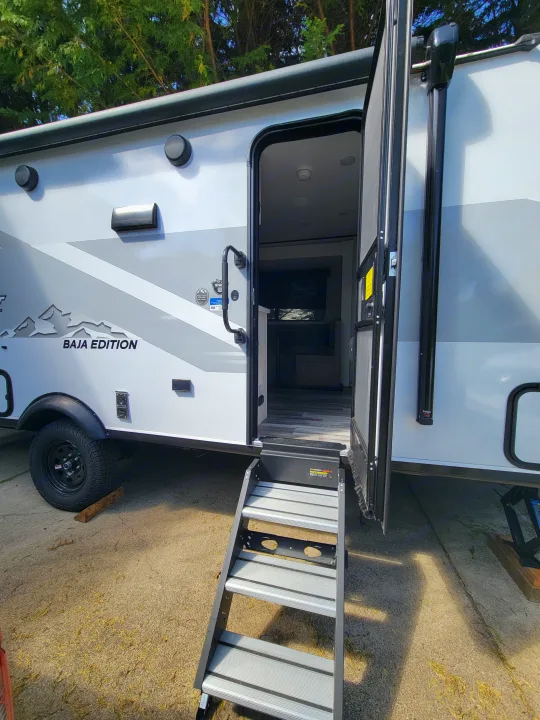 This rv rental, a white Baja Edition travel trailer, features an open door with sturdy silver steps.. Jayco Jay Flight SLX 197MBW Baja Edition 2025