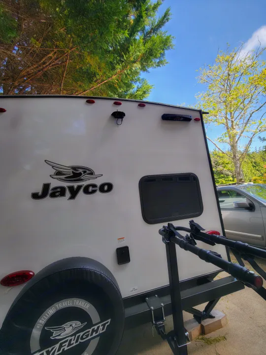 This white Jayco travel trailer RV rental features a rear bike rack for your gear, set against a green tree and blue sky.. Jayco Jay Flight SLX 197MBW Baja Edition 2025