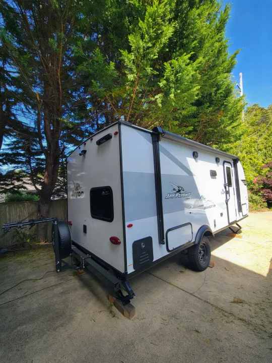 White and gray Jay Flight Baja Edition travel trailer, a compact RV rental option parked on concrete.. Jayco Jay Flight SLX 197MBW Baja Edition 2025