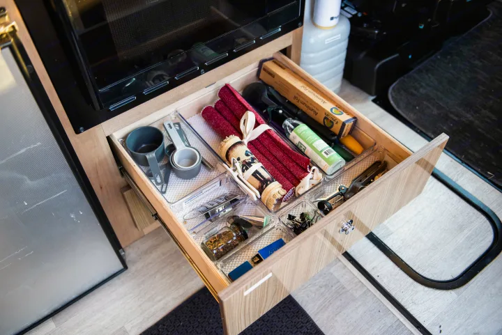 RV rental kitchen drawer, perfectly organized with cooking essentials: foil, measuring cups, and various utensils.. Winnebago Travato 2020