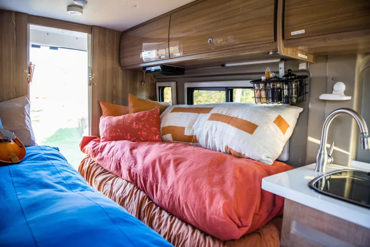Inside a comfy **rv rental**: bed with colorful pillows, kitchen area, and a mandolin for road trip tunes.. Winnebago Travato 2020