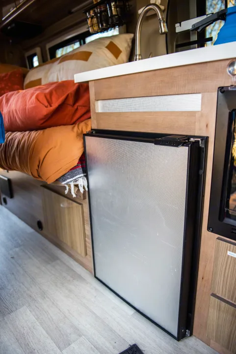 Compact RV rental interior showcasing a modern fridge, sink, and a comfortable bed for road trips.. Winnebago Travato 2020
