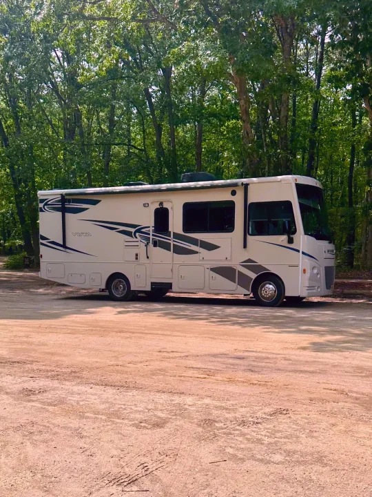 RV rental: A cream Winnebago Vista motorhome parked on a dirt lot in a forest. Ready for adventure.. Winnebago Vista 2018