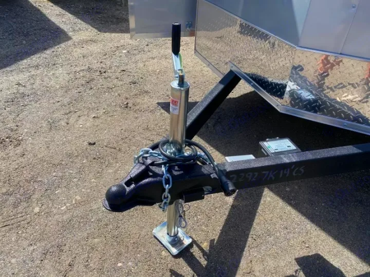 An RV rental trailer's front hitch and jack, with safety chain, visible on gravel. Ready for your next adventure.. ITI Cargo 7X14 2025