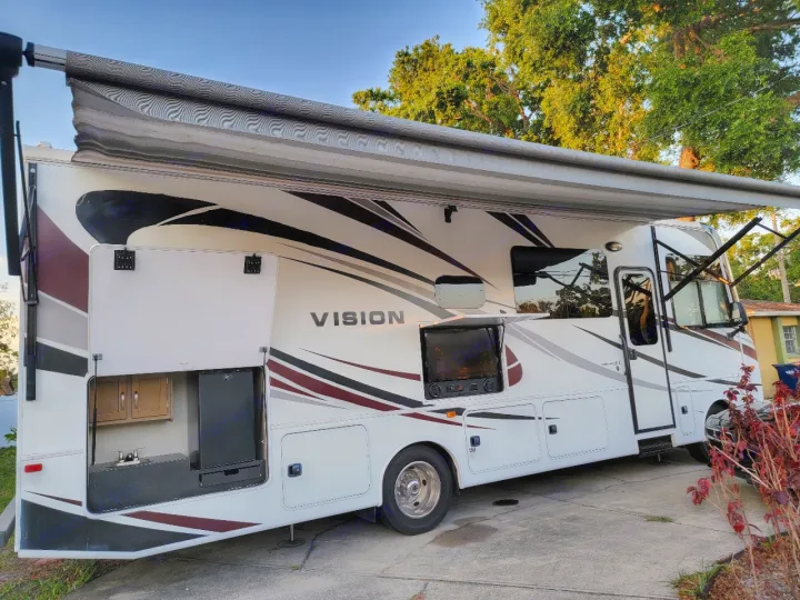 Spacious white RV rental with extended awning, outdoor kitchen, and entertainment setup. Ready for adventure!. Entegra Coach Vision 2019