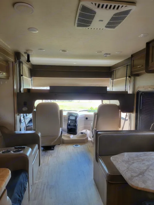 Spacious rv rental interior: driver's area, overhead bunk, and dinette with light wood-look flooring.. Entegra Coach Vision 2019