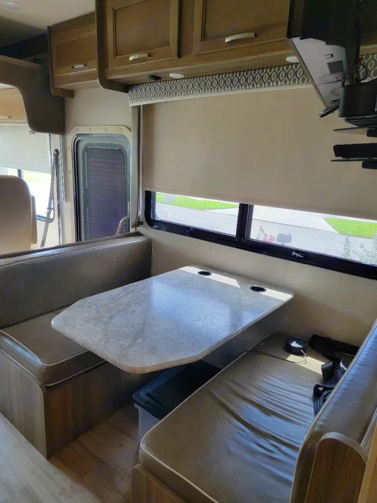 Inside this RV rental: dinette with table, cozy benches, overhead cabinets, and large window with shade.. Entegra Coach Vision 2019