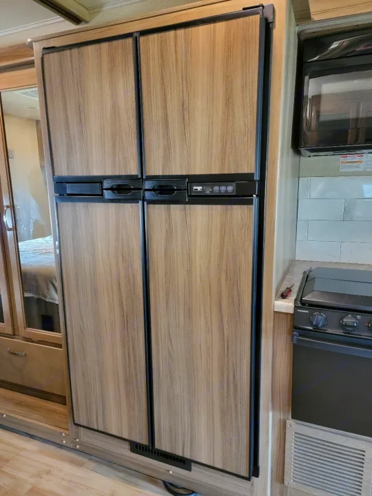 RV rental: Close-up of a functional RV kitchen featuring a large wood-paneled refrigerator, microwave, and stovetop.. Entegra Coach Vision 2019