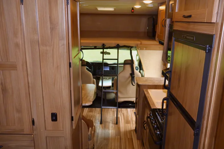 RV rental interior view: Kitchenette with sink, stove, refrigerator, plus overhead bunk ladder and front cockpit. Light wood decor.. Other Freelander 2016