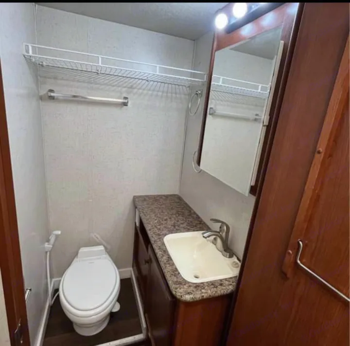 Clean RV rental bathroom with toilet, vanity, sink, mirror, and overhead storage. Ready for your next travel adventure.. Tioga Tioga Motorhome 2009
