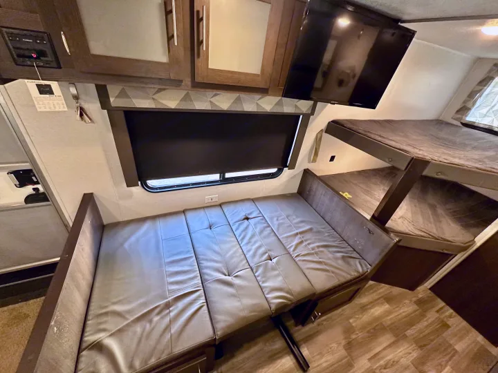 RV rental interior featuring a convertible dinette bed, bunk beds, TV, and overhead storage.. Forest River Wildwood X-Lite 2020