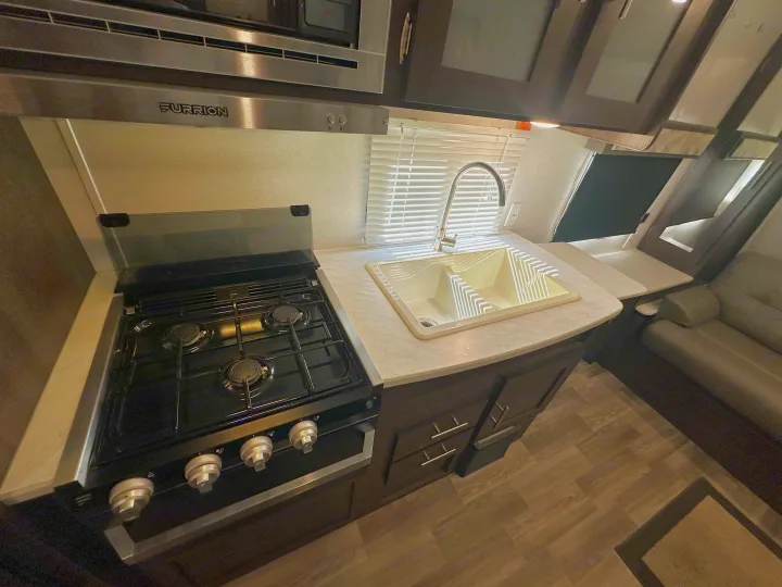 Clean & compact RV rental kitchen featuring a Furrion stove, double sink, and microwave overhead.. Forest River Wildwood X-Lite 2020