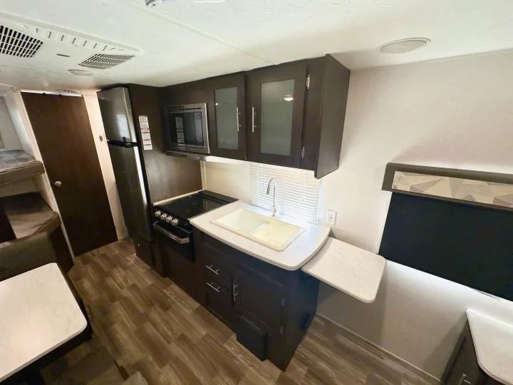 RV rental kitchen: modern design with sink, stove, microwave, fridge, cabinets & dining. Compact and functional interior.. Forest River Wildwood X-Lite 2020