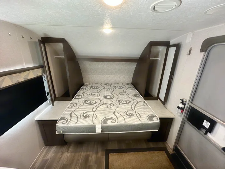 RV rental bedroom: patterned bed, dark wood cabinets, side counters, and overhead storage for a functional space.. Forest River Wildwood X-Lite 2020