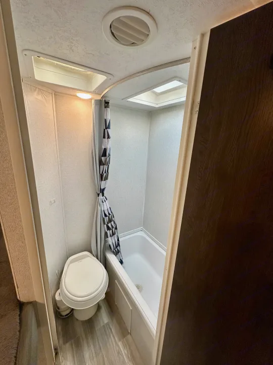 Compact RV rental bathroom featuring a toilet, tub/shower with curtain, and ceiling vents/skylights.. Forest River Wildwood X-Lite 2020