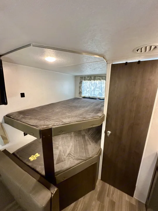Inside an RV rental: comfortable bunk beds with a window, a door, and an AC vent. Ideal for family camping.. Forest River Wildwood X-Lite 2020