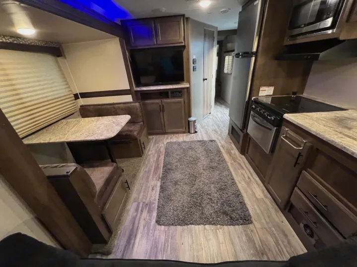 This RV rental interior offers a comfortable dinette, full kitchen, and entertainment center, all on wood-look flooring.. KZ Connect RLK 24 2019