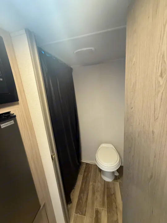 This RV rental features a compact bathroom with a toilet and shower curtain, next to a small Everchill fridge.. Heartland Pioneer 2025