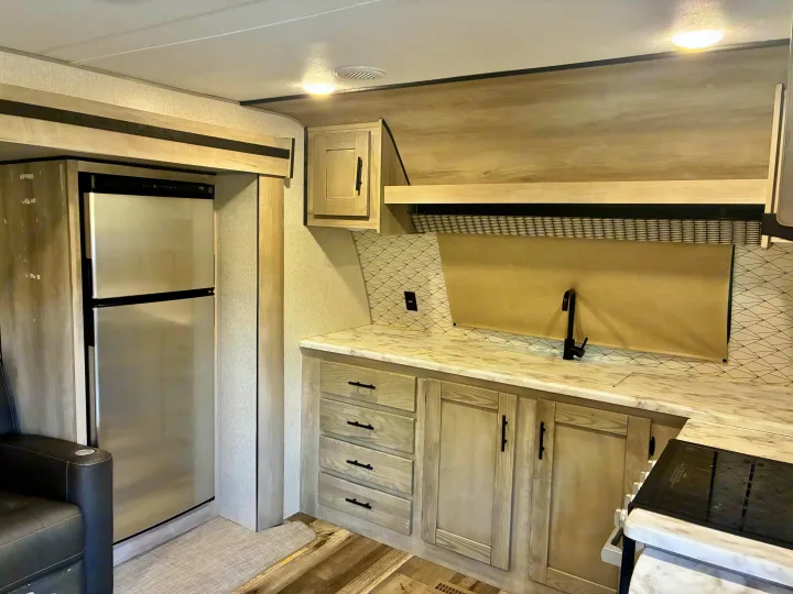 Modern RV rental interior showcasing a well-equipped kitchen with fridge, sink, and stovetop.. KZ Connect SE 2024