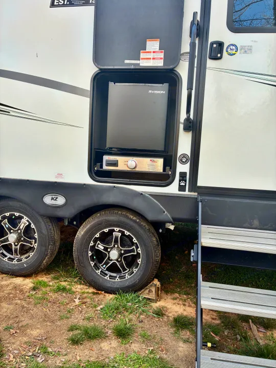An RV rental's exterior panel opens to reveal an outdoor kitchen setup with a Suburban grill and RVISION fridge.. KZ Connect SE 2024