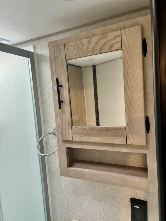 Compact RV rental bathroom featuring a light wood mirror cabinet, open shelf, and frosted shower door.. KZ Connect SE 2024
