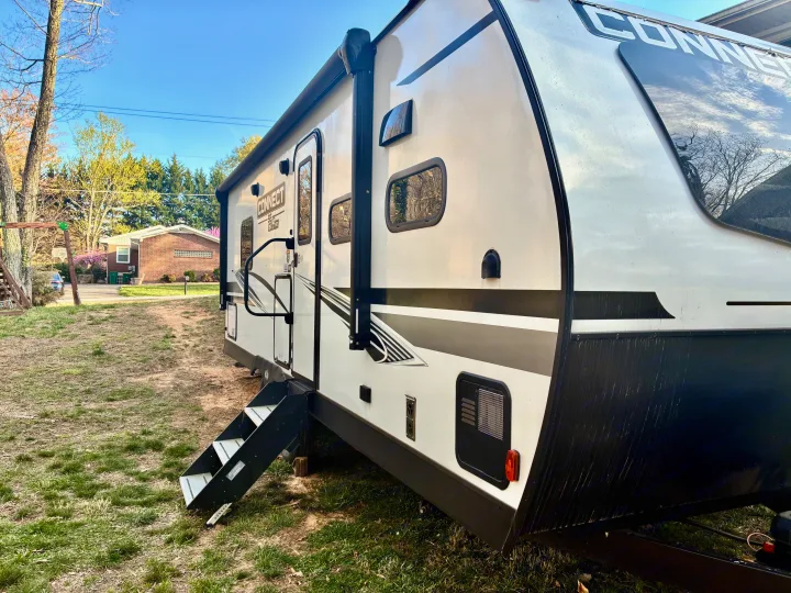 Exterior view of a white and black Connect RV rental parked on a residential lawn, with steps extended.. KZ Connect SE 2024