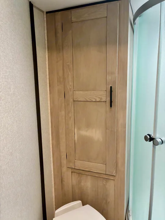 Compact RV rental bathroom showcasing light wood storage unit, frosted shower door, and toilet.. KZ Connect SE 2024