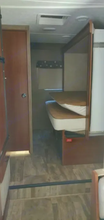 Inside an RV rental, a cozy sleeping area features two bunk beds (one folded), a wooden door, and patterned floor.. Forest River Forester 2017