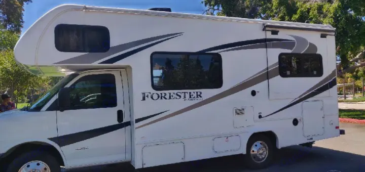 White Forester Class C RV rental, displaying graphics, windows, and an awning; parked outdoors.. Forest River Forester 2017