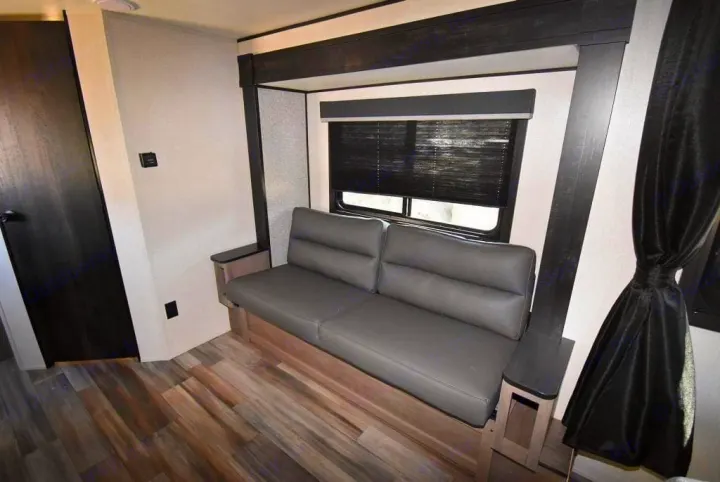 Modern RV rental living space featuring a comfortable gray sofa, window with dark blinds, and stylish wood-look flooring.. Starcraft Autumn Ridge 20FBS 2022