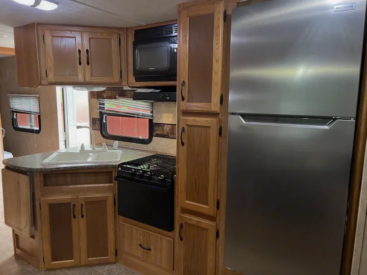 Well-equipped RV rental kitchen featuring a stainless steel fridge, wood cabinets, stove, and double sink.. Keystone RV Sprinter Select 2010