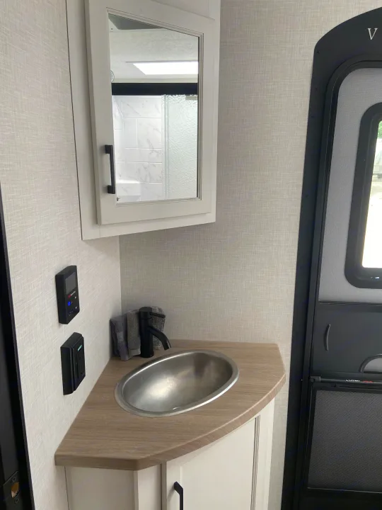 RV rental interior: A compact bathroom featuring a stainless steel sink, black faucet, mirrored cabinet, and wall controls near the entrance.. Venture Rv Sporttrek 2026