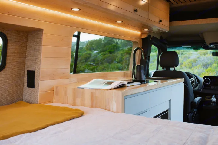 Cozy RV rental interior: compact kitchen, comfortable bed, and scenic window for travel.. Mercedes-Benz Sprinter 2025