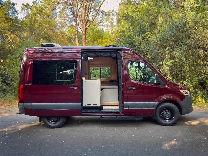 Burgundy camper van, perfect for rv rental, with its side door open showing a light, modern custom interior.. Mercedes-Benz Sprinter 2025