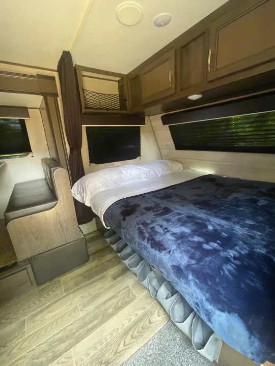 RV rental interior: a comfy bed with under-bed storage, small dinette, overhead cabinets, and wood-look flooring.. Jayco Jay Flight SLX 2021