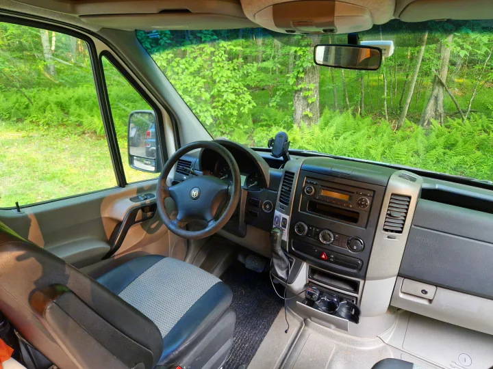 Driver's view from an rv rental: a detailed look at the van's cockpit, dashboard, and vibrant forest outside.. Dodge Sprinter Van 2008