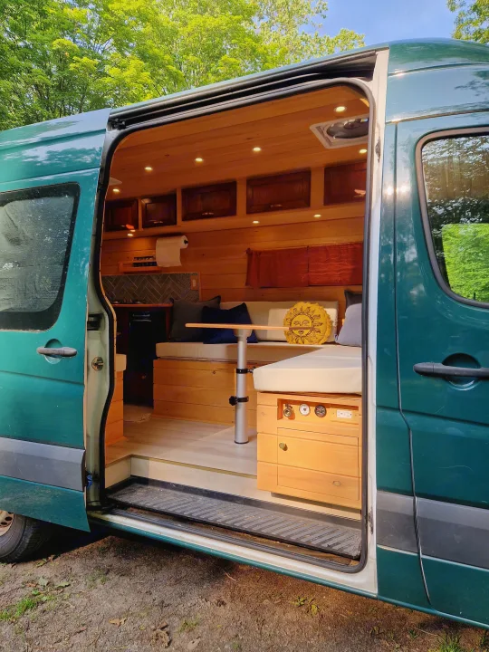 Interior of a teal custom van conversion, revealing a cozy wooden living space for rv rental.. Dodge Sprinter Van 2008