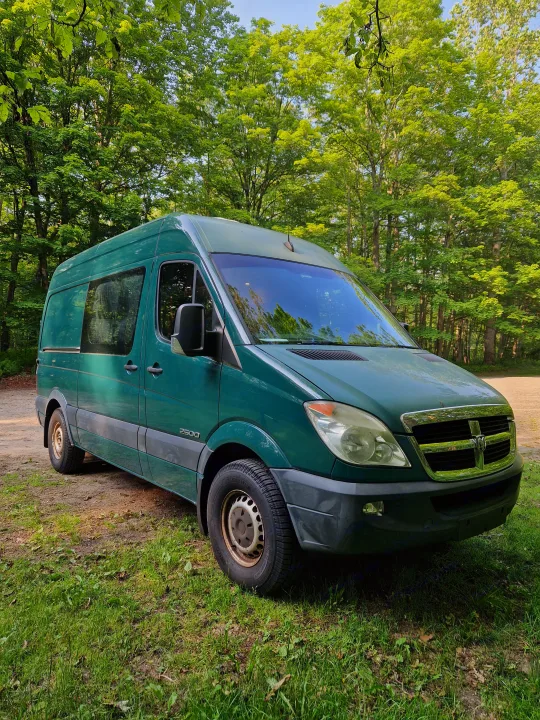 Green Dodge Sprinter camper van, great for an RV rental, parked in a sunny, tree-filled forest.. Dodge Sprinter Van 2008
