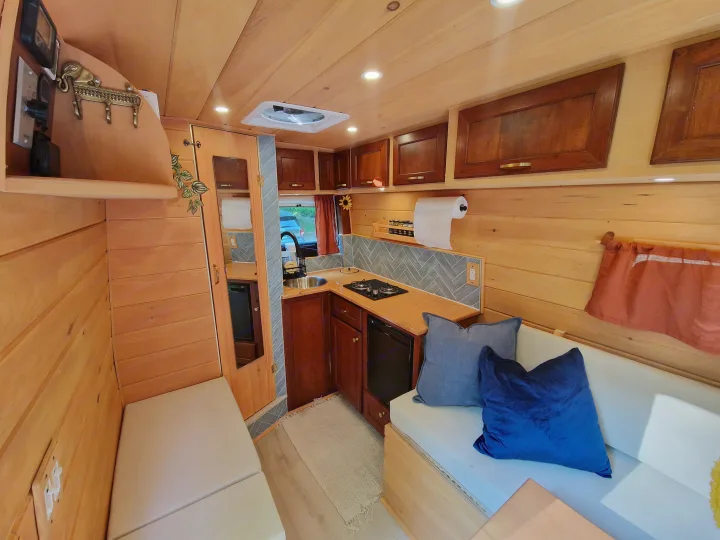 Explore this warm RV rental interior: light wood, functional kitchen with stove & sink, cozy seating, and ample storage.. Dodge Sprinter Van 2008