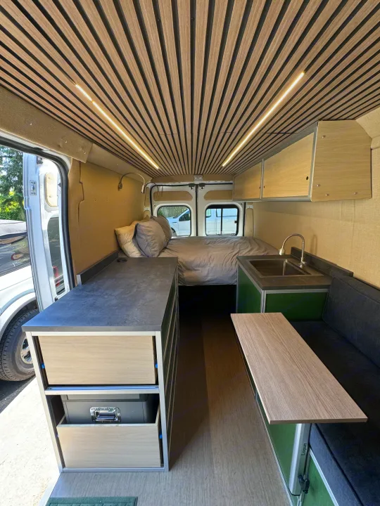 Step inside this modern RV rental: a compact living space with a bed, kitchen, custom storage, and stylish wood accents.. Dodge B Van 2023