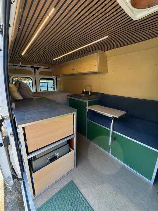 Stylish RV rental: This camper van features a wood-slat ceiling, full bed, kitchen, and dinette with table.. Dodge B Van 2023