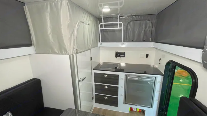 Inside a modern RV rental: Features a compact kitchen with sink/fridge, sofa seating, and pop-top roof.. Zoomies Campers Eagle’s Nest 2025