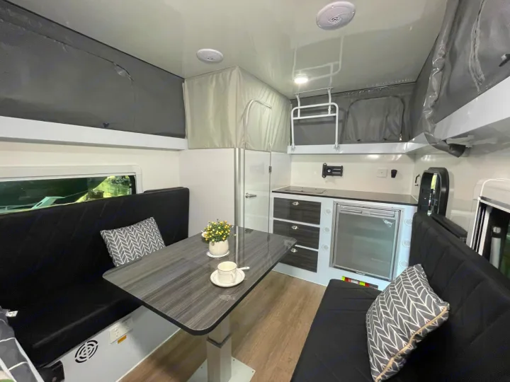 Modern RV rental interior with dining benches, kitchen, and bunk beds overhead. Ideal for family adventures.. Zoomies Campers Eagle’s Nest 2025