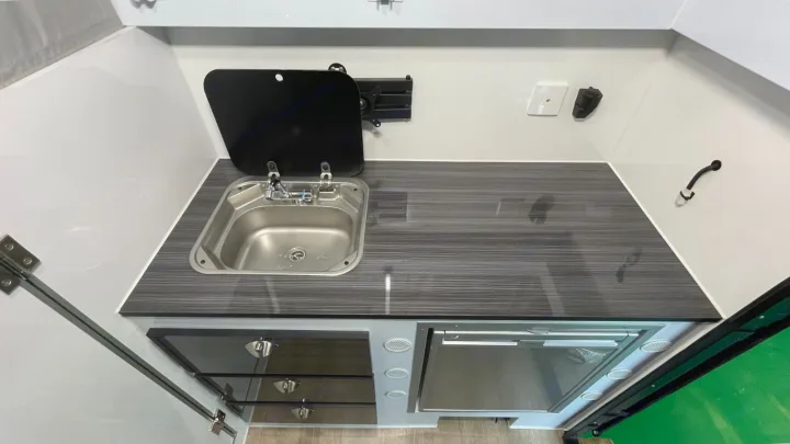 This compact RV rental kitchen features a stainless steel sink, dark wood-grain countertop, and integrated appliances.. Zoomies Campers Eagle’s Nest 2025