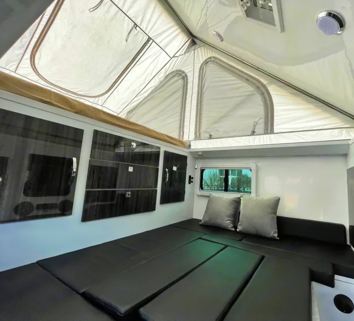 Inside a modern RV rental: a bright pop-up roof, black padded seating that converts to a bed, and wall storage.. Zoomies Campers Spirit 2025