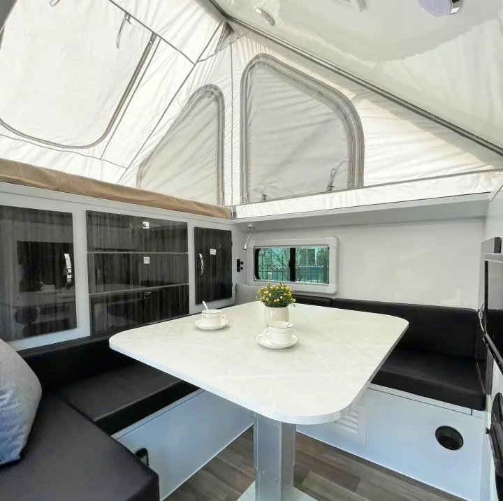 Cozy RV rental interior: pop-top roof, dinette with light table, black seating, and modern storage cabinets.. Zoomies Campers Spirit 2025